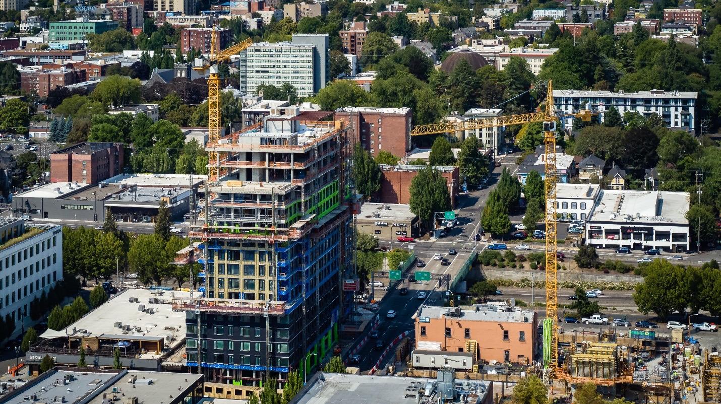 A photo taken over the city showing a high-rise building being built surround by scaffolds and cranes.